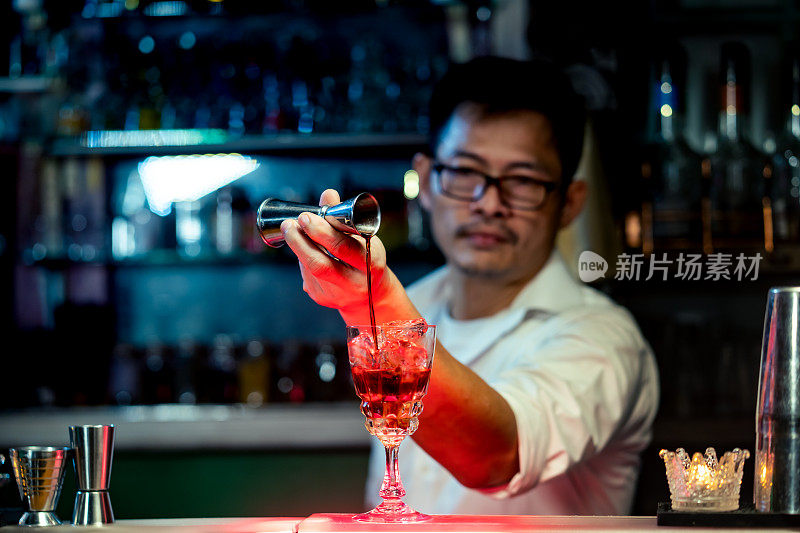 Professional barman pouring liquor from jigger into cocktail glass on counter bar for preparing mixed alcoholic drink to serving in nightclub party. Male mixologist bartender making cocktail drink at bar